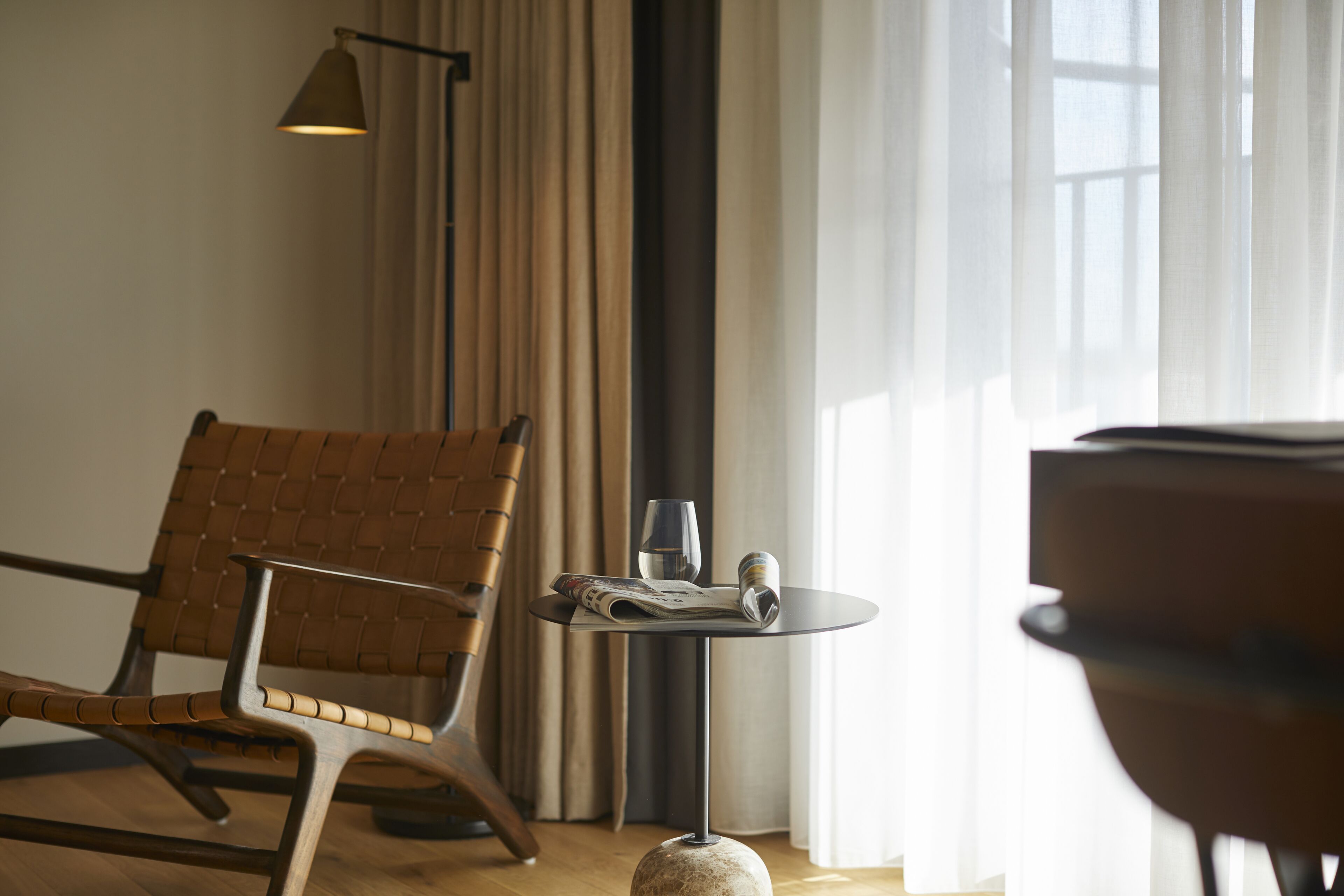 Een moderne kamer met een houten stoel, een klein rond tafeltje met een krant, glazen en een boek.