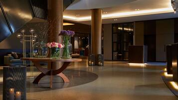 Eine moderne Lobby mit einem zentralen Tisch, der Vasen und Kerzen präsentiert, umgeben von Sitzgelegenheiten und einer großen Säule.