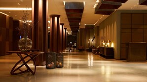 A spacious, well-lit hallway with wooden columns, a reception desk, and a seating area with tables and chairs.