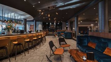 Uma área de bar moderna com um bartender, banquetas e um espaço de estar com um sofá e cadeiras.