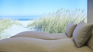 A bed with a view of the beach and sea.