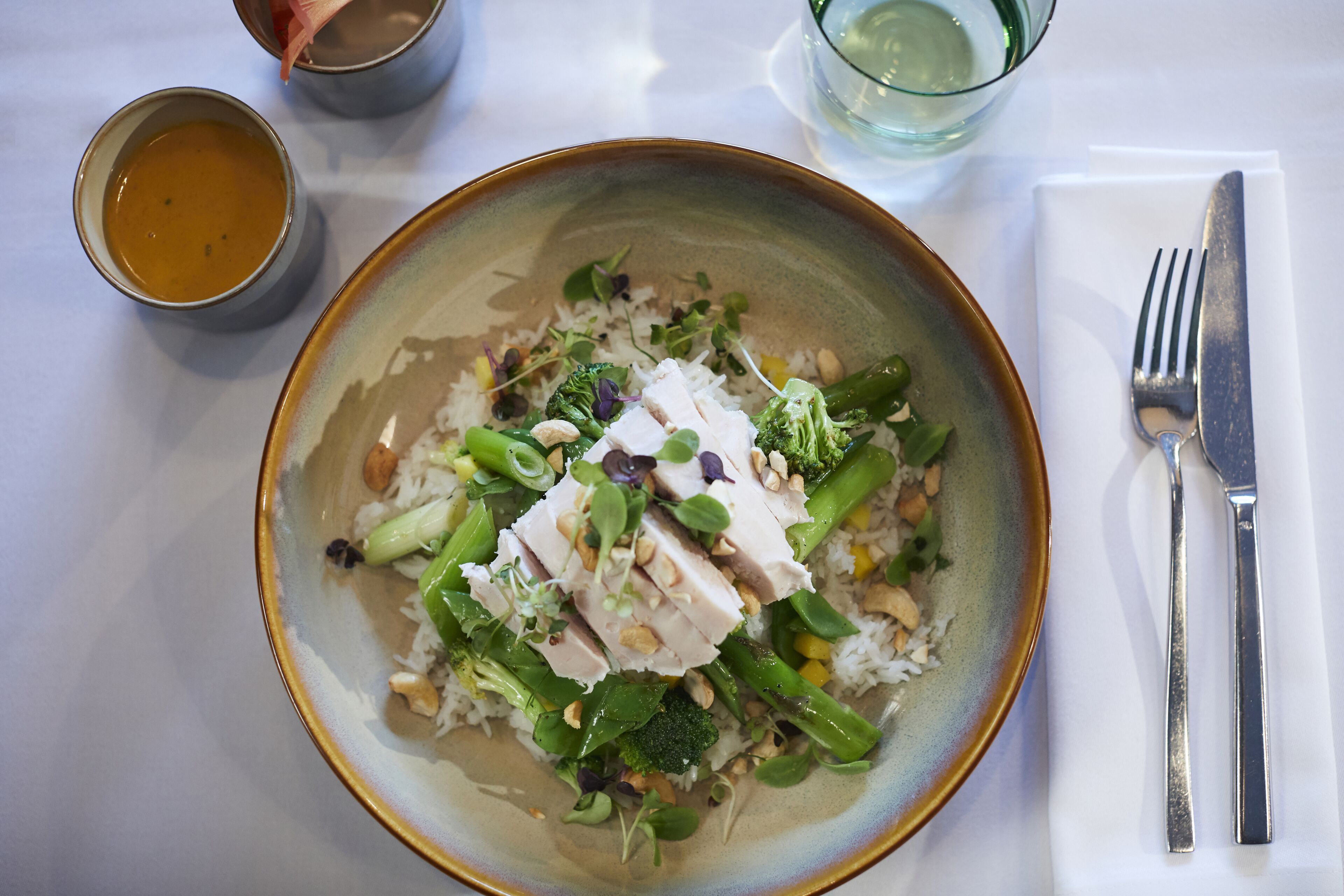 Un bol rempli de nourriture, contenant du riz, des légumes et du poulet, est posé sur une table.