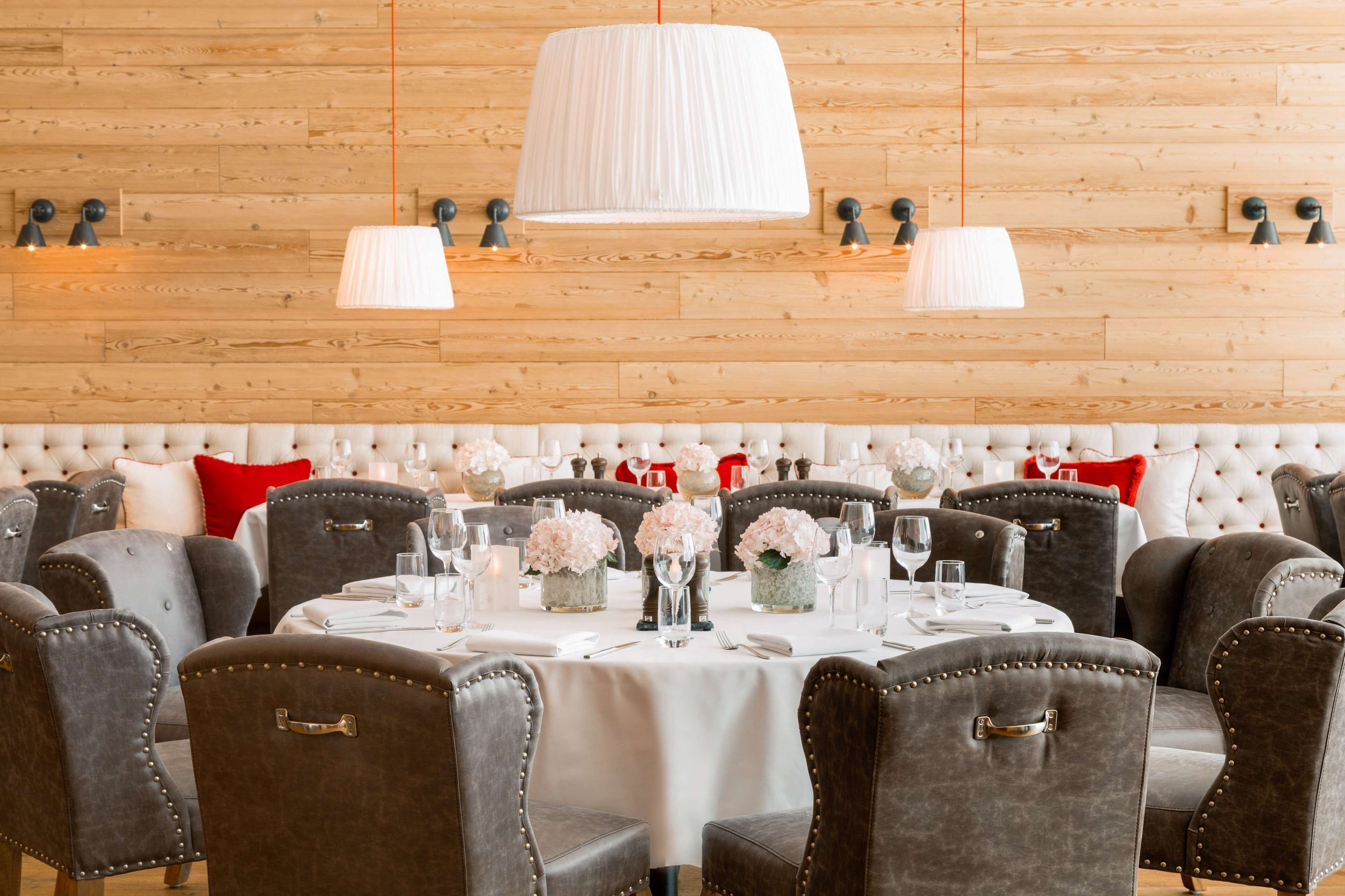 Un comedor con mesas redondas cubiertas con manteles blancos, sillas tapizadas en gris y lámparas blancas.