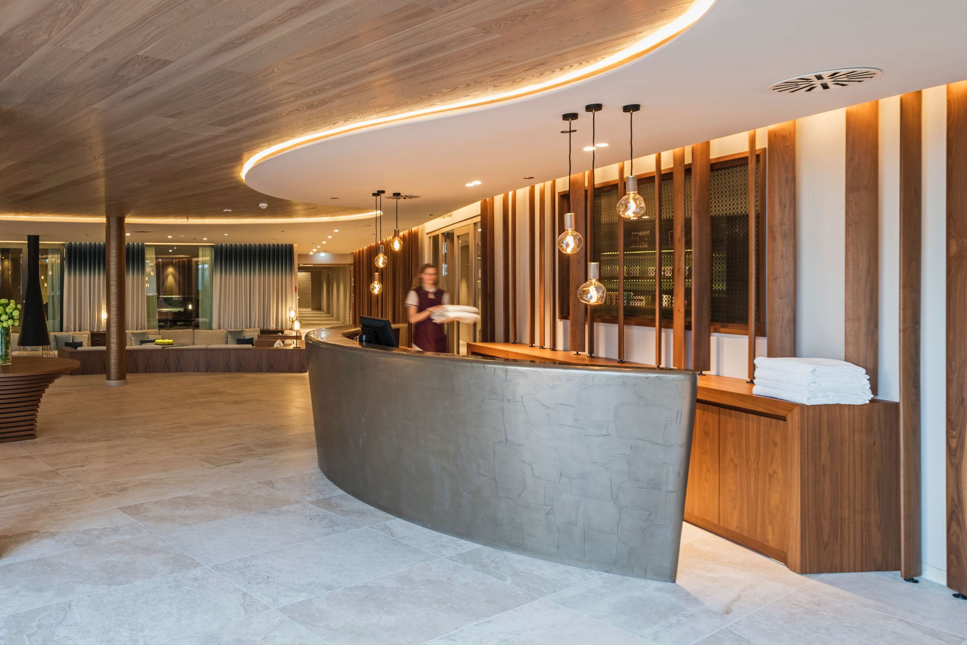 A modern reception area with a curved reception desk, wooden paneling, and hanging pendant lights.