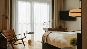 A hotel room with a bed, a chair, a desk, a TV, and a window with curtains.