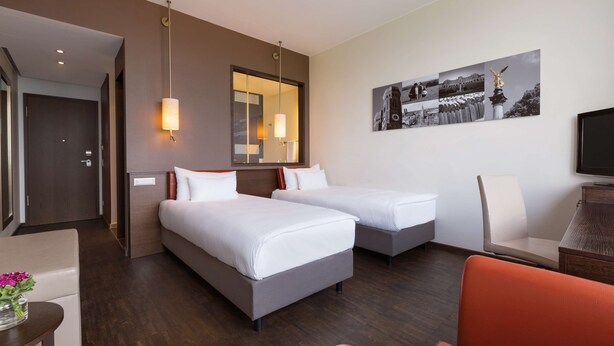 A hotel room with two beds, a desk, a chair, and a television. - Infinity Hotel & Conference Resort Munich (Unterschleissheim)