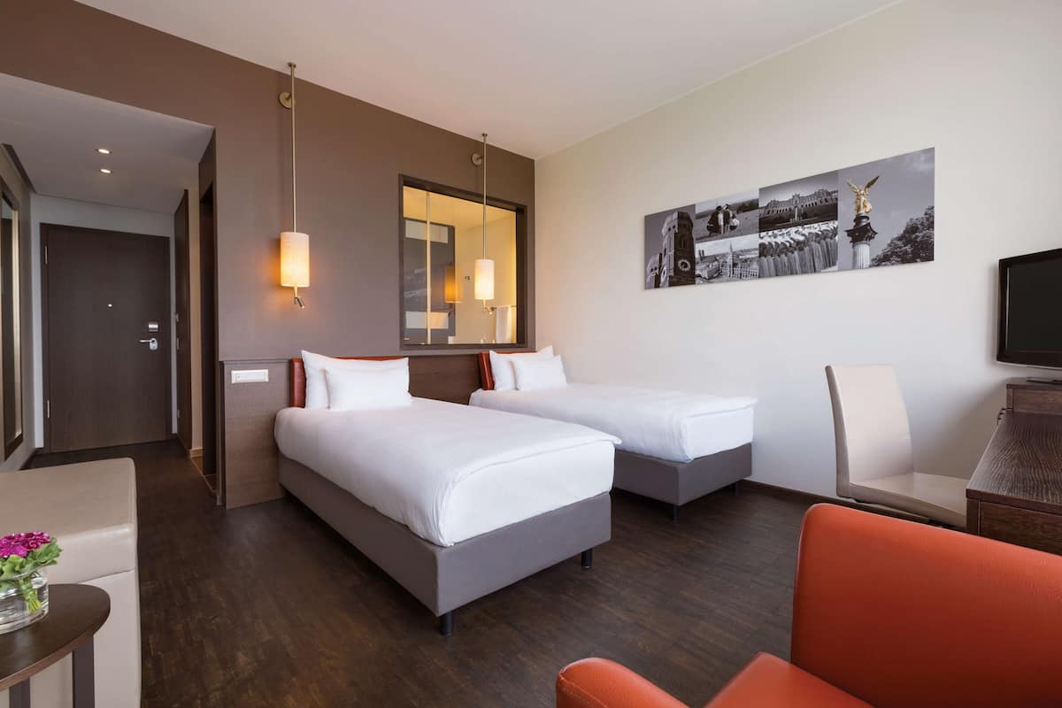 Une chambre d’hôtel avec deux lits, un bureau, une chaise et un téléviseur.