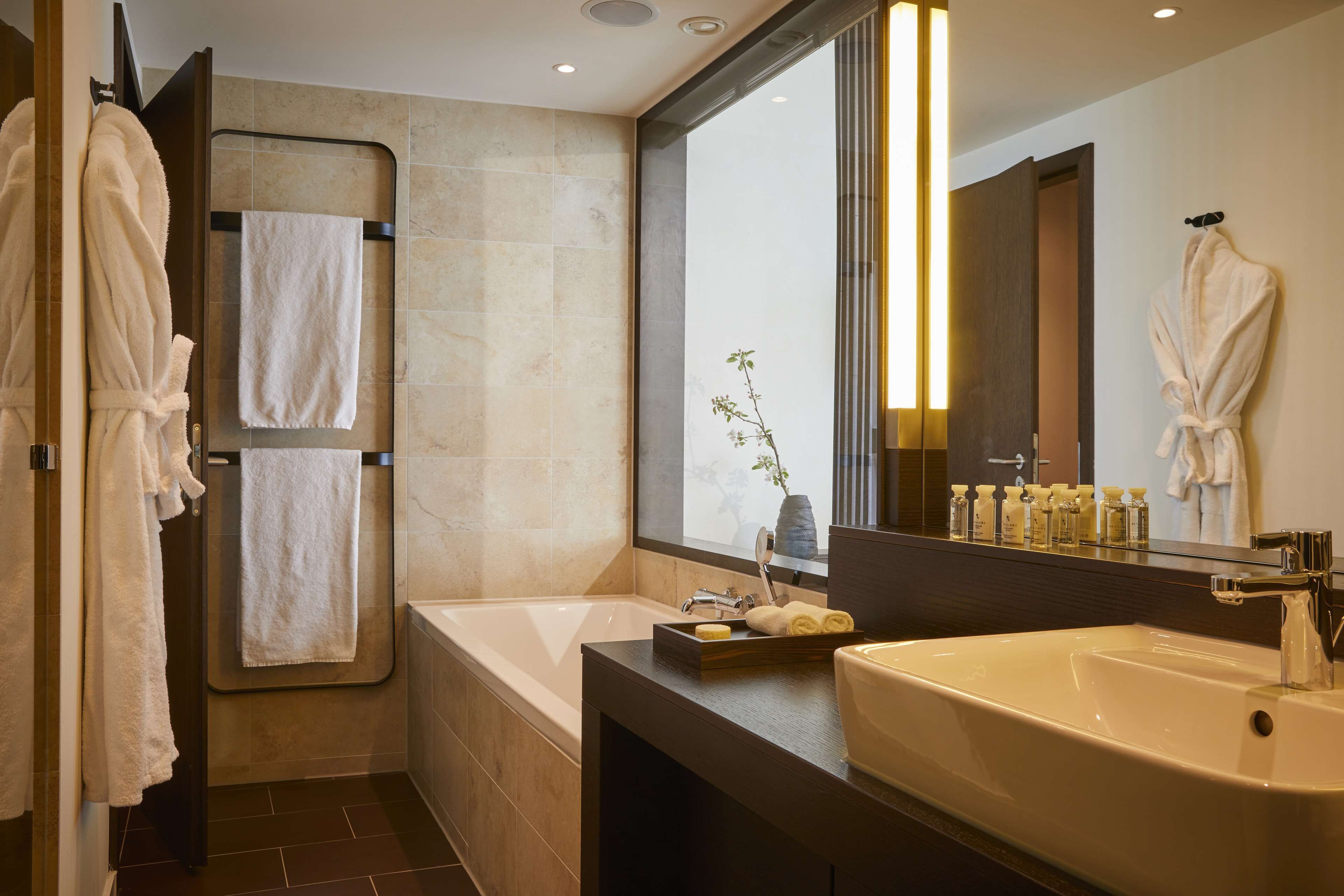 A modern bathroom with a bathtub, a large mirror, and a vanity with toiletries.