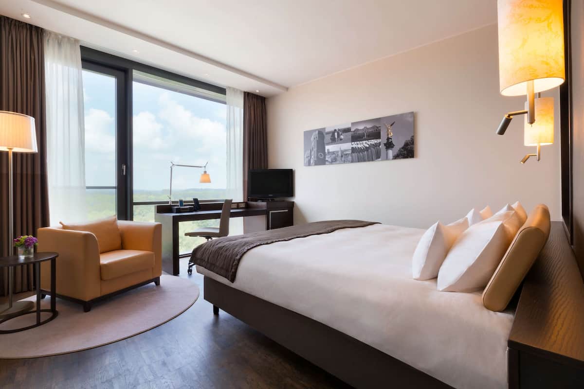 Une chambre d’hôtel avec un grand lit, un bureau, une chaise, une télévision et une fenêtre donnant sur un beau paysage.