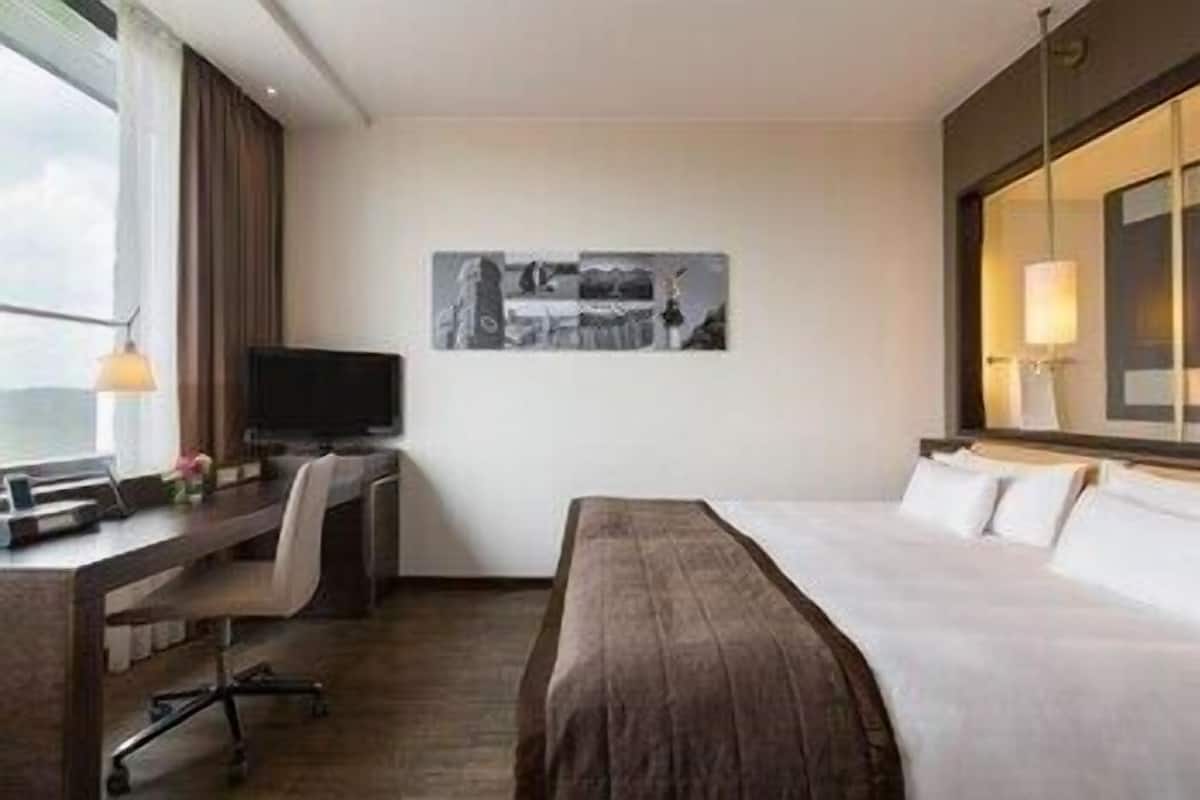 Une chambre d’hôtel avec un lit, un bureau avec un ordinateur, une télévision et une fenêtre.