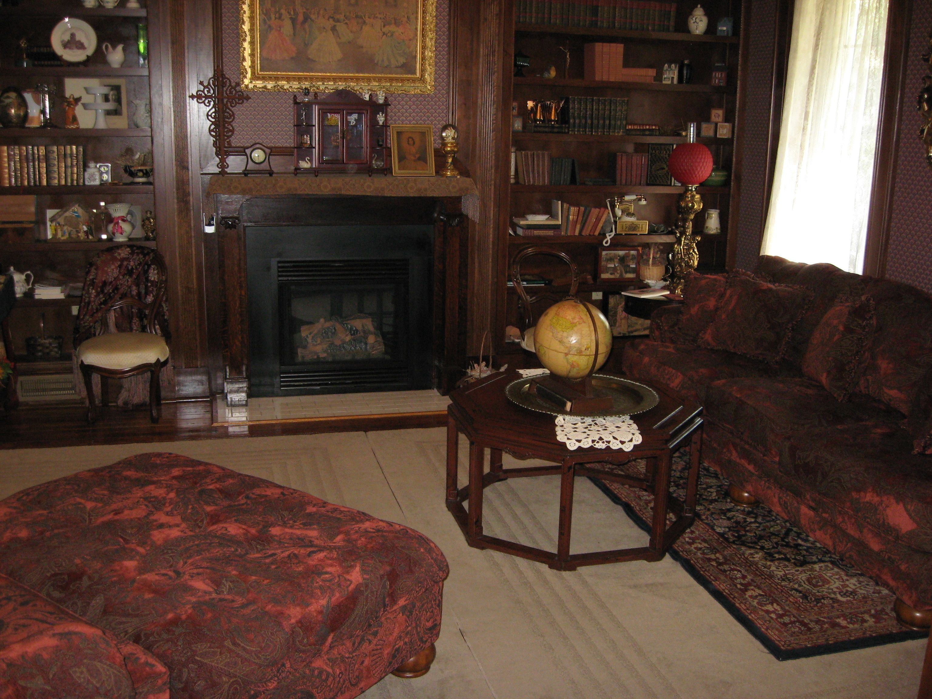 Un salón tradicional con chimenea, un sofá, un sillón y una estantería llena de libros y objetos decorativos.