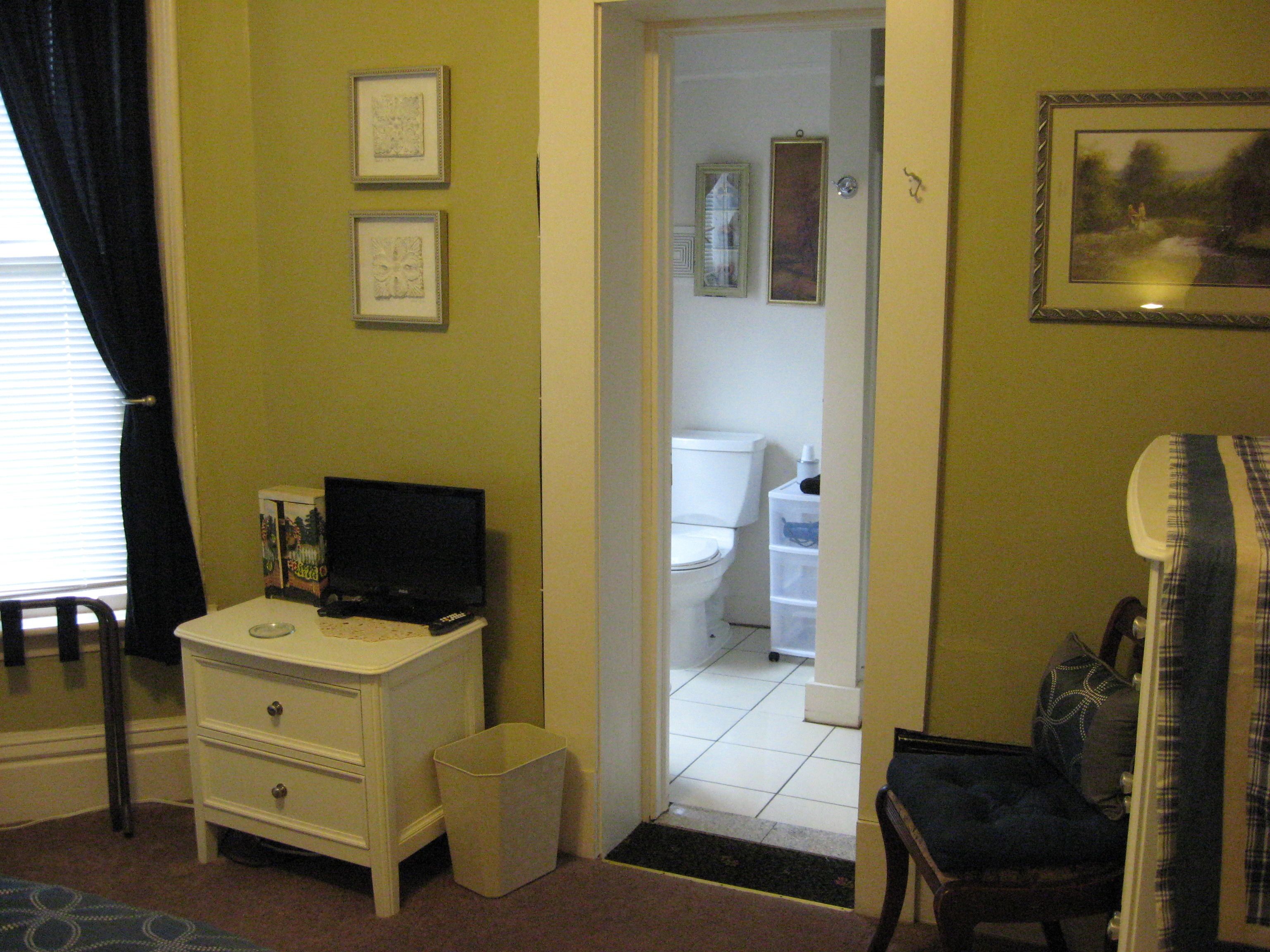 A room with a white dresser, a television, a framed picture on the wall, and a door leading to a bathroom.