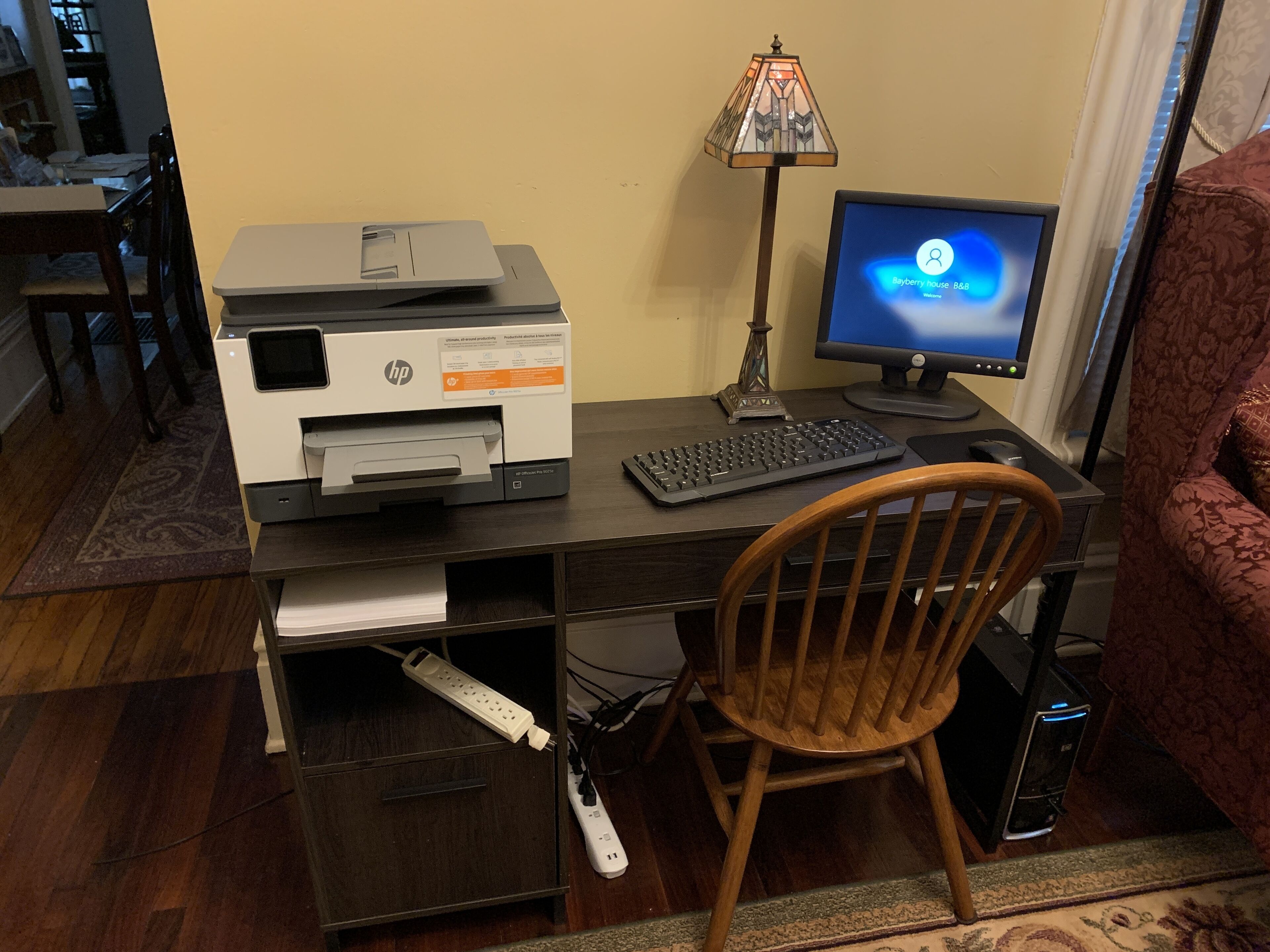 A home office setup with a printer, monitor, keyboard, and chair.