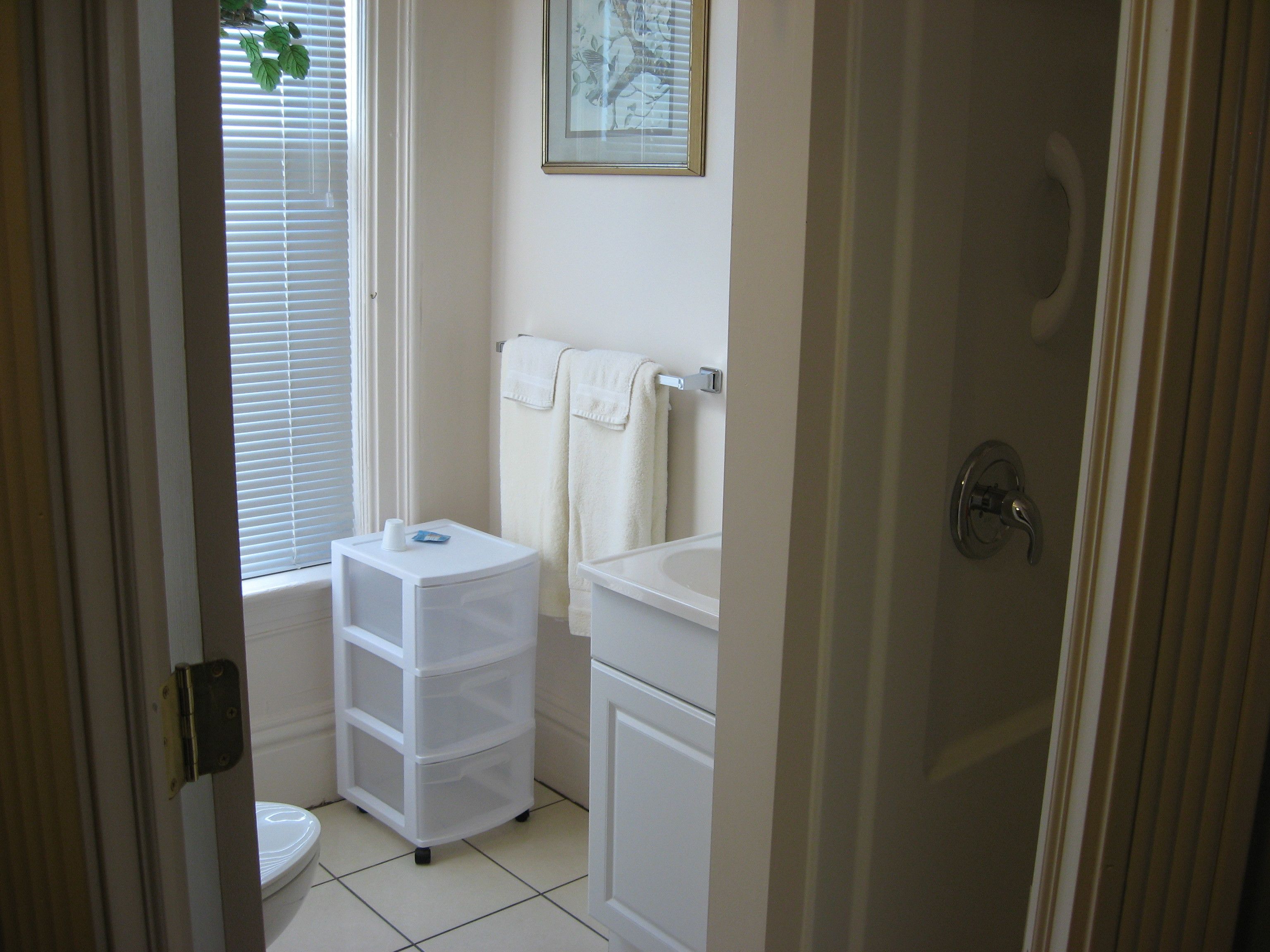 A bathroom with a toilet, a sink, a white cabinet, a white towel rack, and a small white storage unit with drawers.