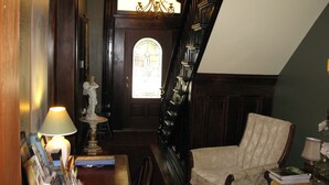 Een houten trap met een kroonluchter, een stoel en een tafel met boeken en een lamp.