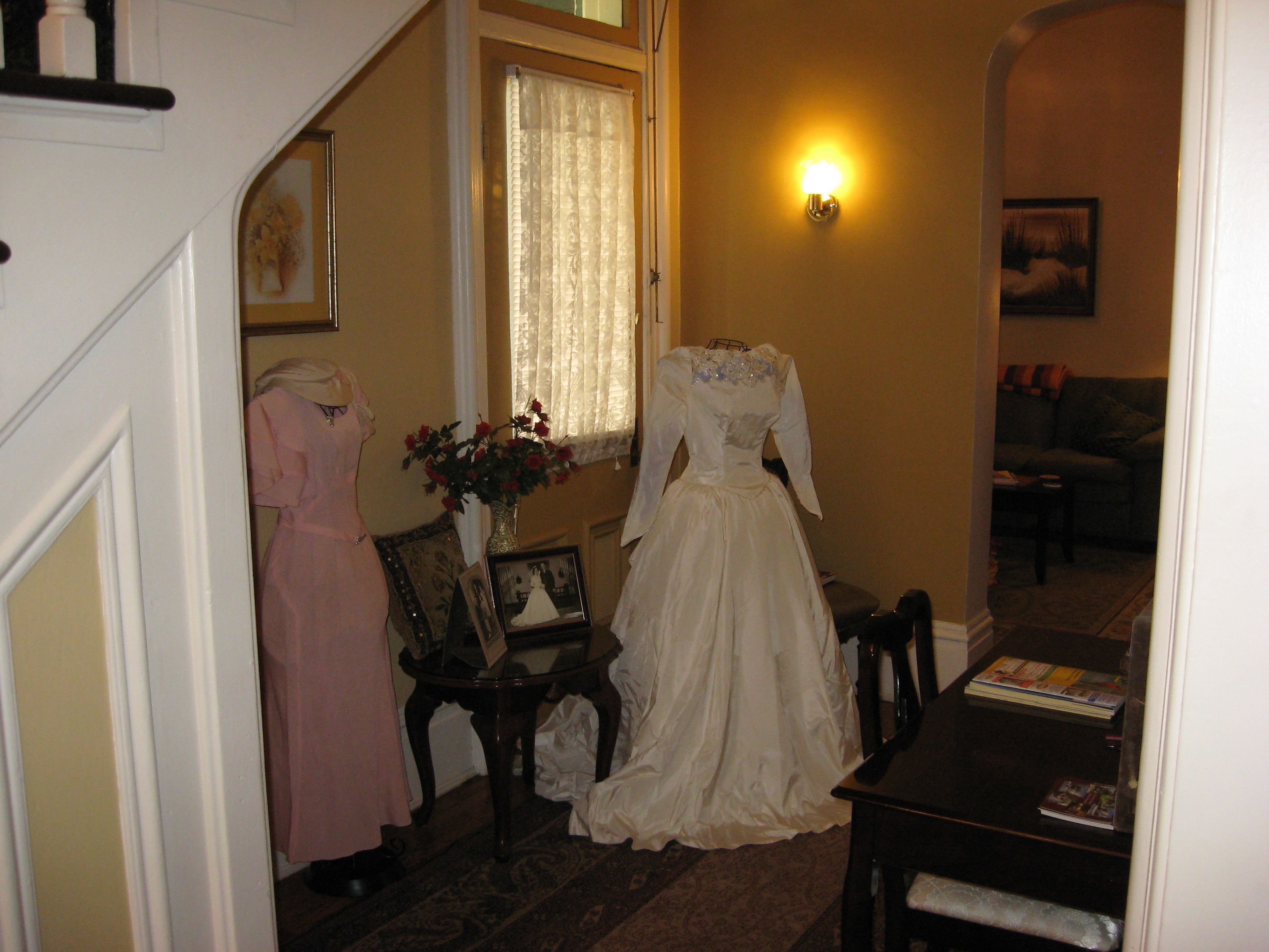 A room with a dining table, a vase with flowers, and two dresses on mannequins.