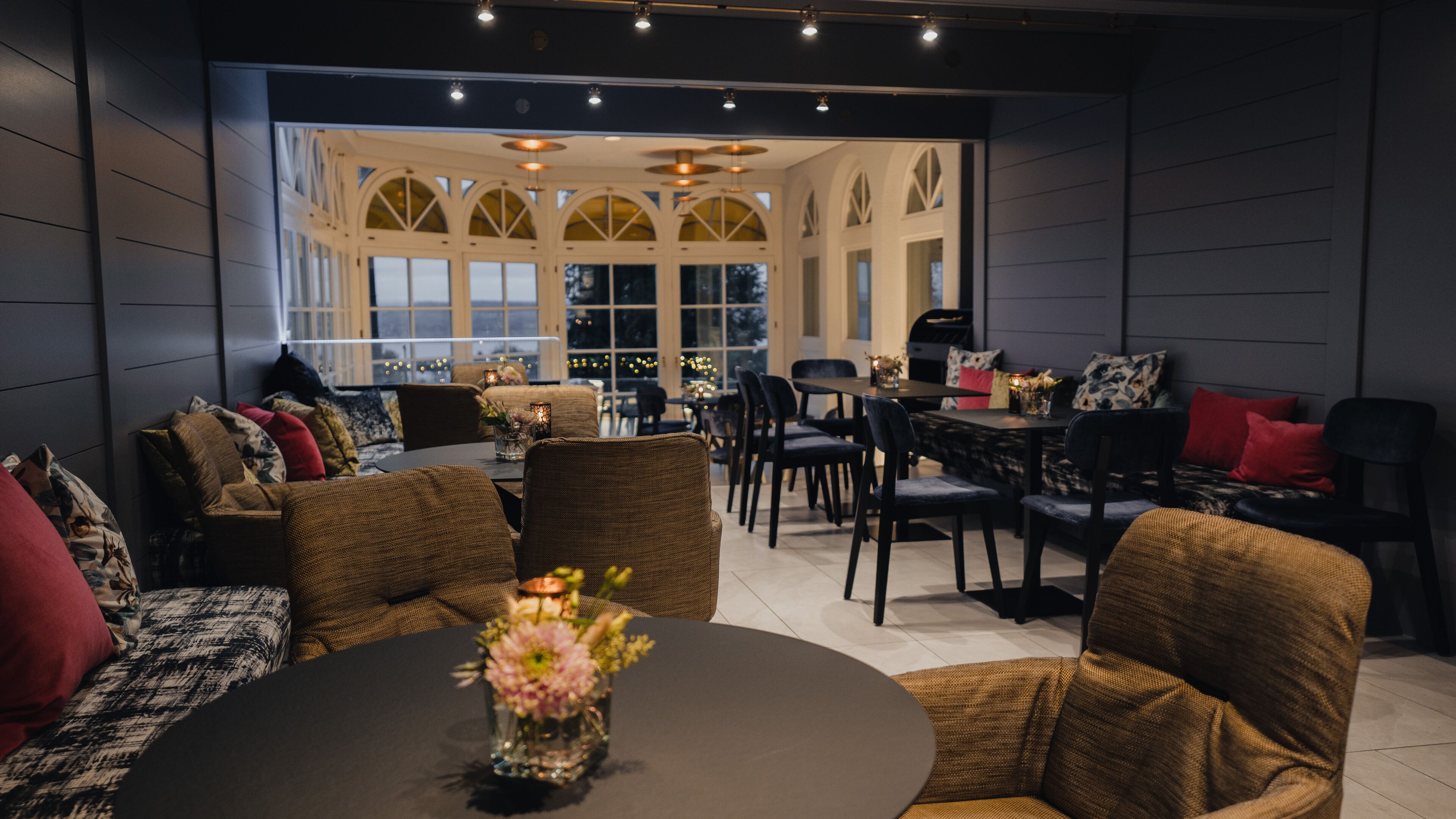 Interior moderno com paredes escuras, móveis de vime e uma mesa redonda central com um vaso de flores.
