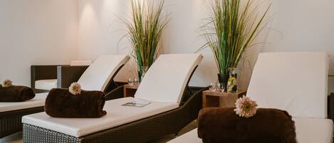 A spa area with reclining chairs, each with a towel and a flower. There are two tall plants in vases.