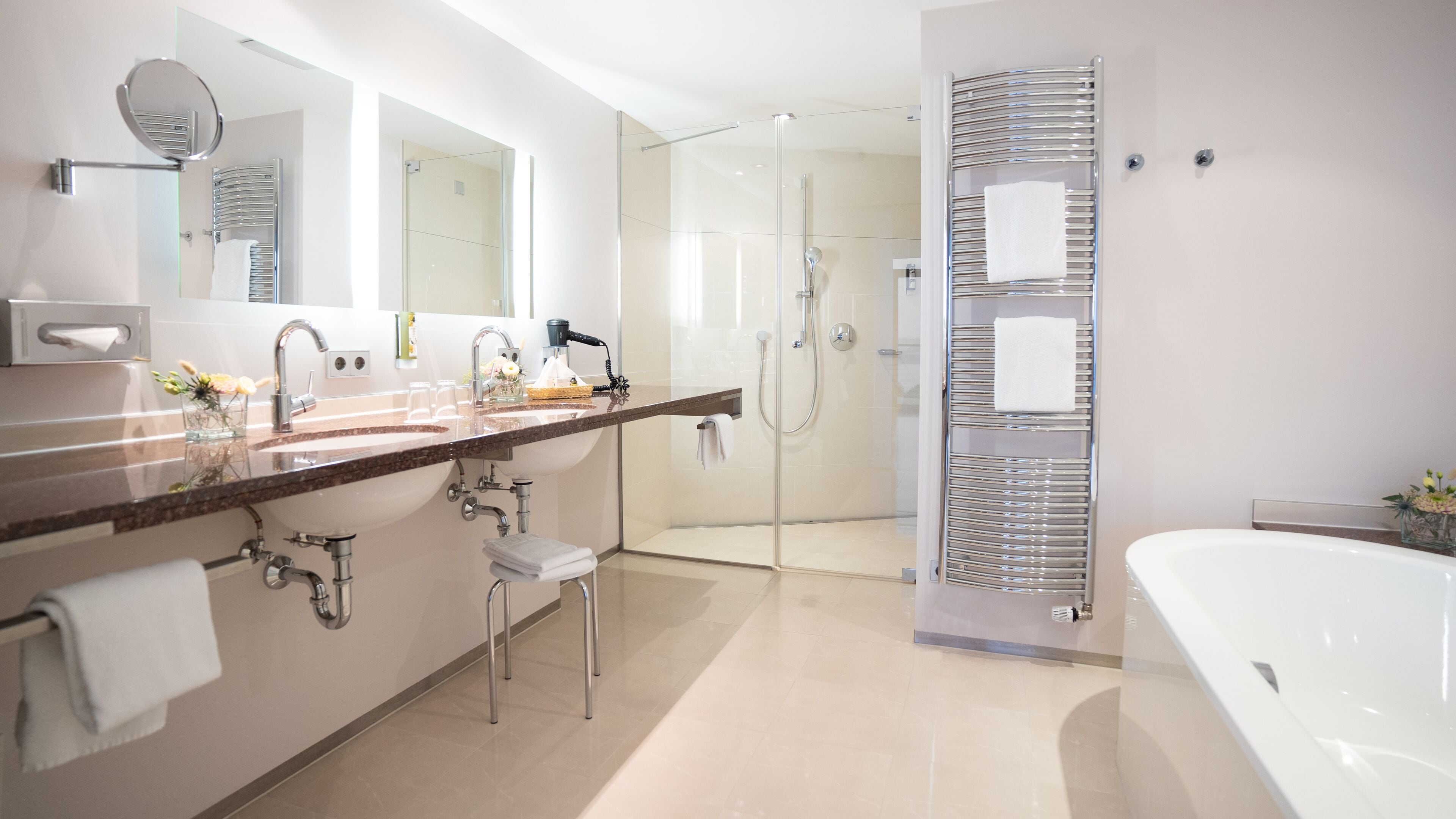 A modern bathroom with a large white bathtub, a glass-enclosed shower, and a vanity with a mirror and multiple sinks.