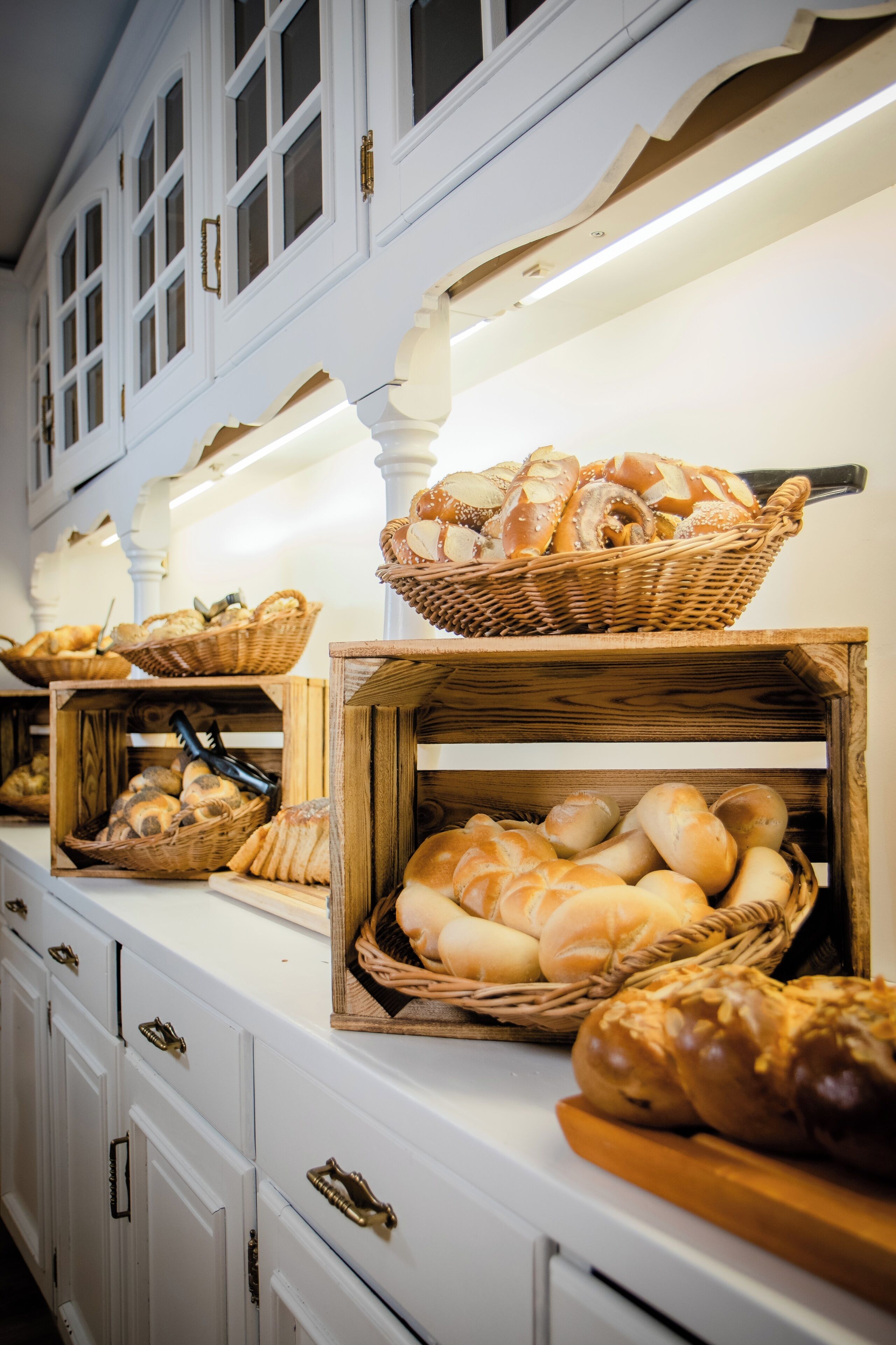 Een buffetopstelling met diverse broden en gebak, gepresenteerd in rieten manden en houten kisten.