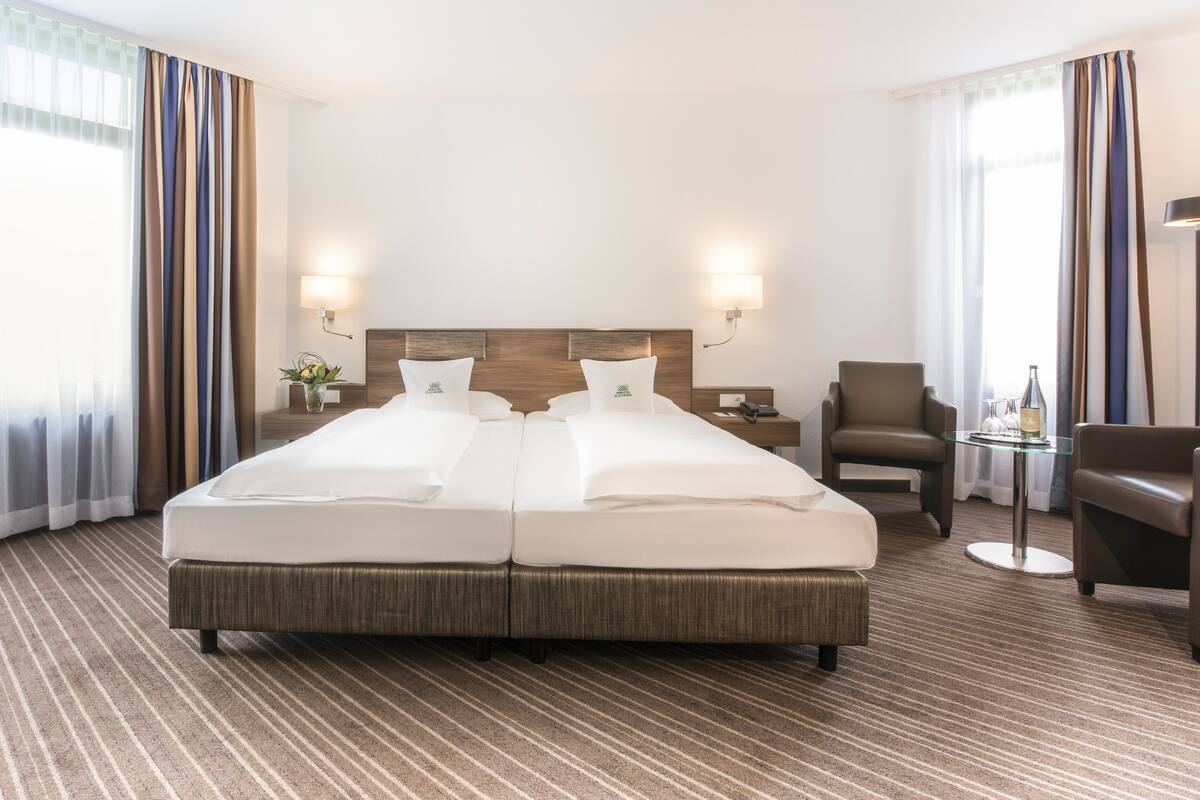 A hotel room with a large bed, two bedside tables, a chair, a small table with a lamp, and curtains.