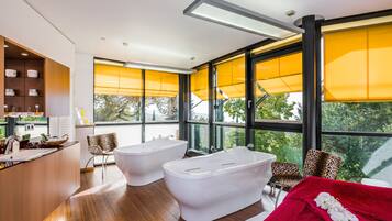 Ein modernes Badezimmer mit zwei weißen Wannen, Holzboden und großen Fenstern mit gelben Jalousien.