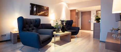 Un salon moderne avec deux canapés sombres, une table basse et un tableau accroché au mur.