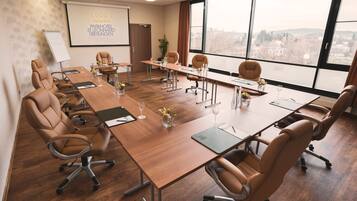 Un salón de conferencias con una larga mesa, sillas de cuero, una pizarra y un amplio ventanal con vistas a la ciudad.
