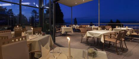 An outdoor dining area with tables set for two, featuring candles and wine glasses.