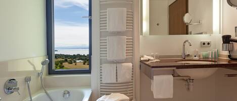 Un baño moderno con bañera, ducha, tocador con espejo y ventana con vistas al exterior.
