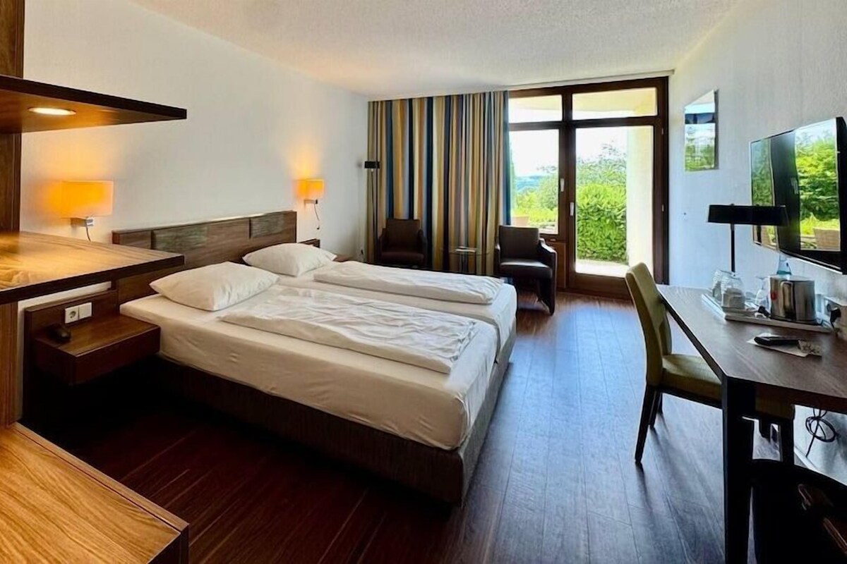 Una habitación de hotel con cama, escritorio, silla, televisor y ventana con vistas.