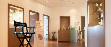 A hotel reception area with a wooden floor, a reception desk, a chair, and a glass display case.