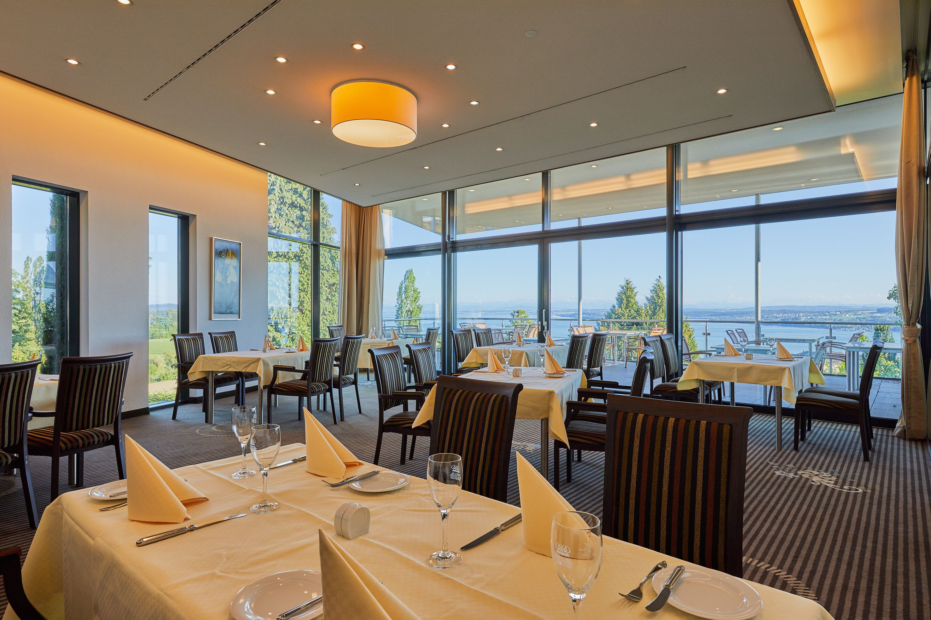 A restaurant with tables set for dining, large windows offering a view of the outdoors, and a modern interior design.