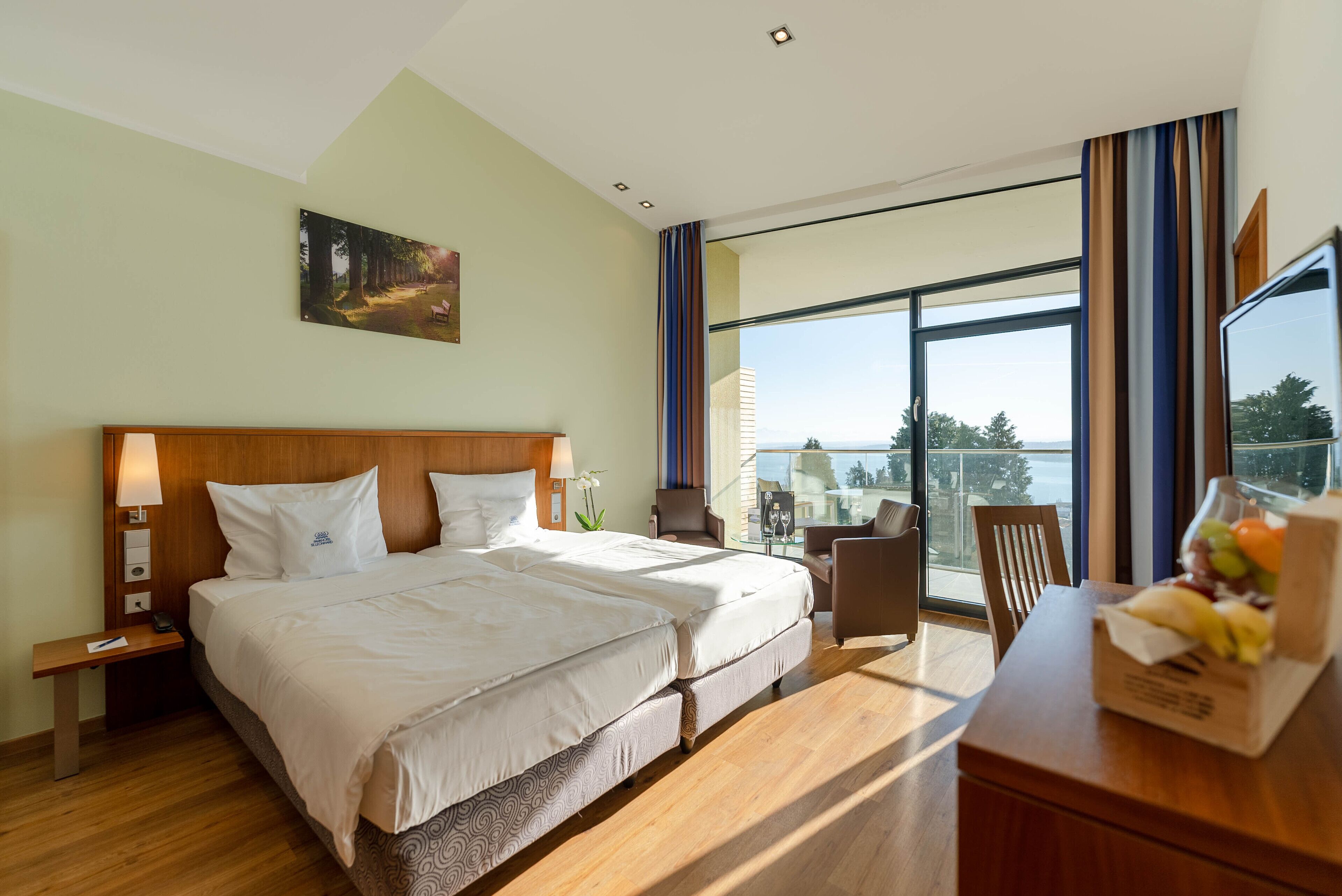 Une chambre d’hôtel avec un grand lit, un bureau agrémenté d’un panier de fruits, une chaise et une vue sur l’extérieur.