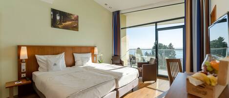 Une chambre d’hôtel avec un grand lit, un bureau agrémenté d’un panier de fruits, une chaise et une vue sur l’extérieur.