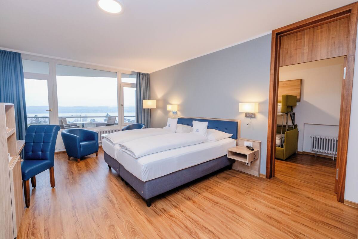 A hotel room with a large bed, two armchairs, a desk, and a view of the city.