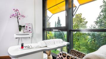 A modern room with a large window, a white desk with a lamp, a leopard print chair, and a view of greenery outside.