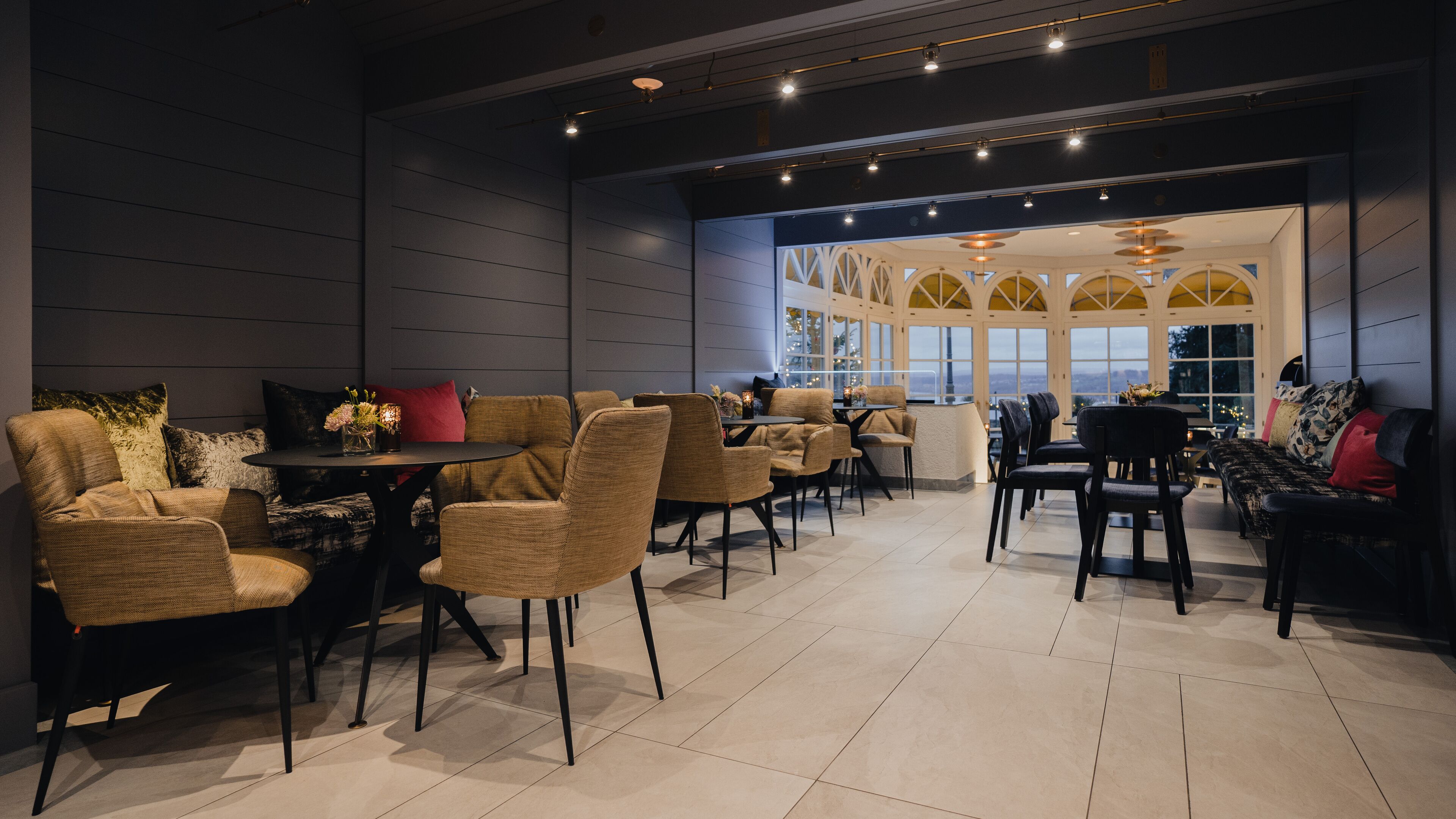 Un área de estar moderna con diversas opciones de asientos, incluyendo sofás y sillones, una zona de bar y grandes ventanales con vistas a la ciudad.