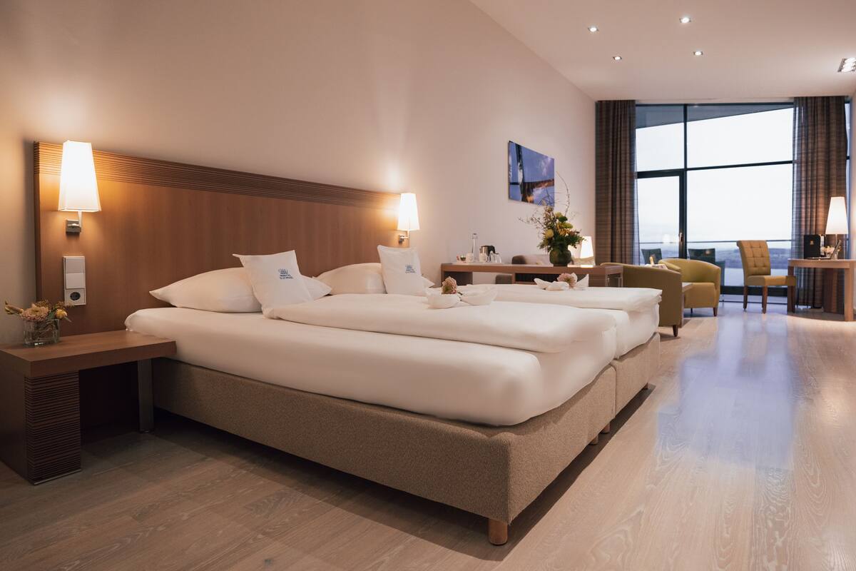 A hotel room with a large bed, bedside tables, a desk, a chair, and a TV.