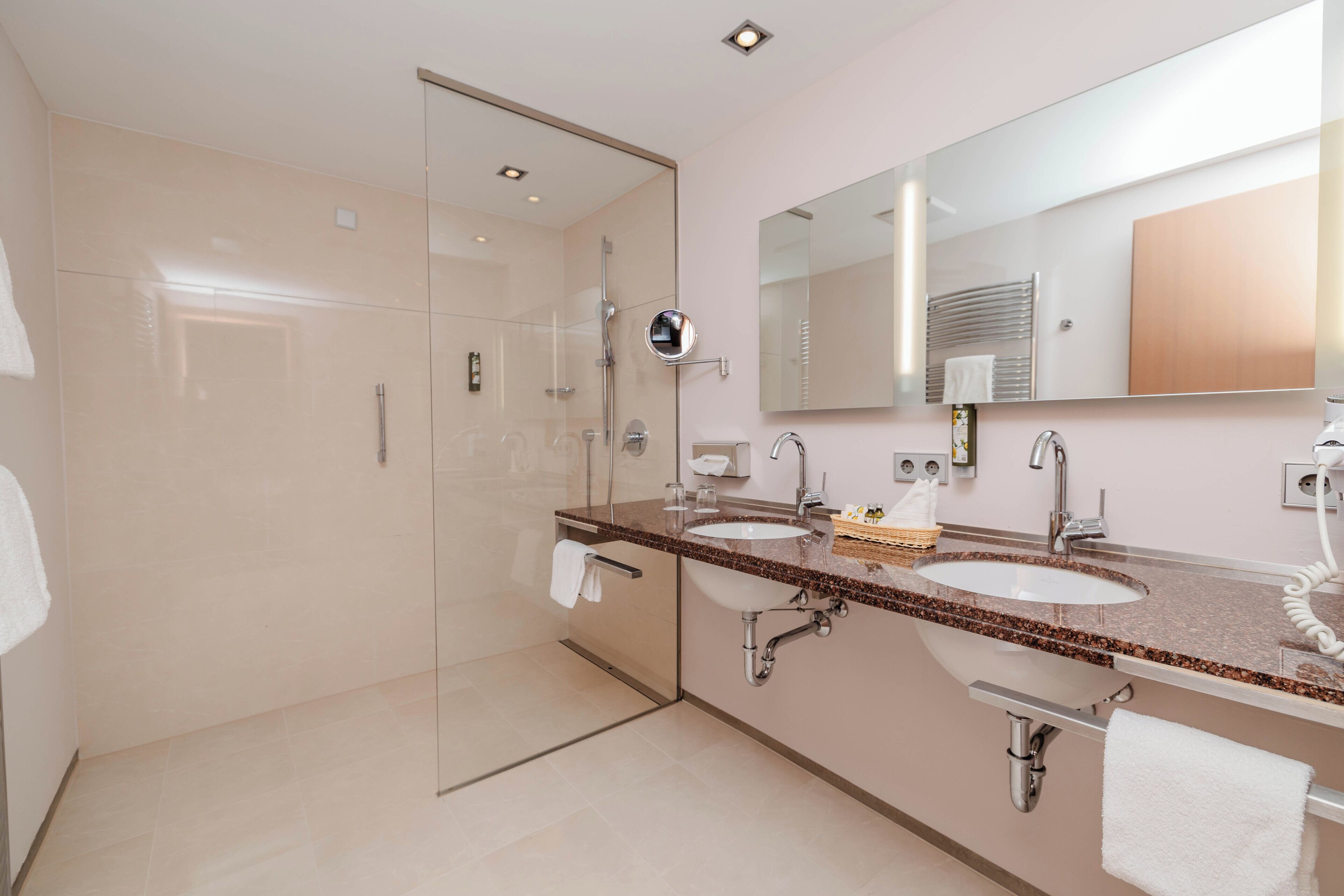 Un baño moderno con dos lavamanos, cabina de ducha con vidrio y un espejo grande.