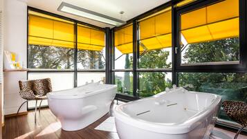 Ein modernes Badezimmer mit zwei freistehenden Badewannen, großen Fenstern mit gelben Jalousien und Holzboden.