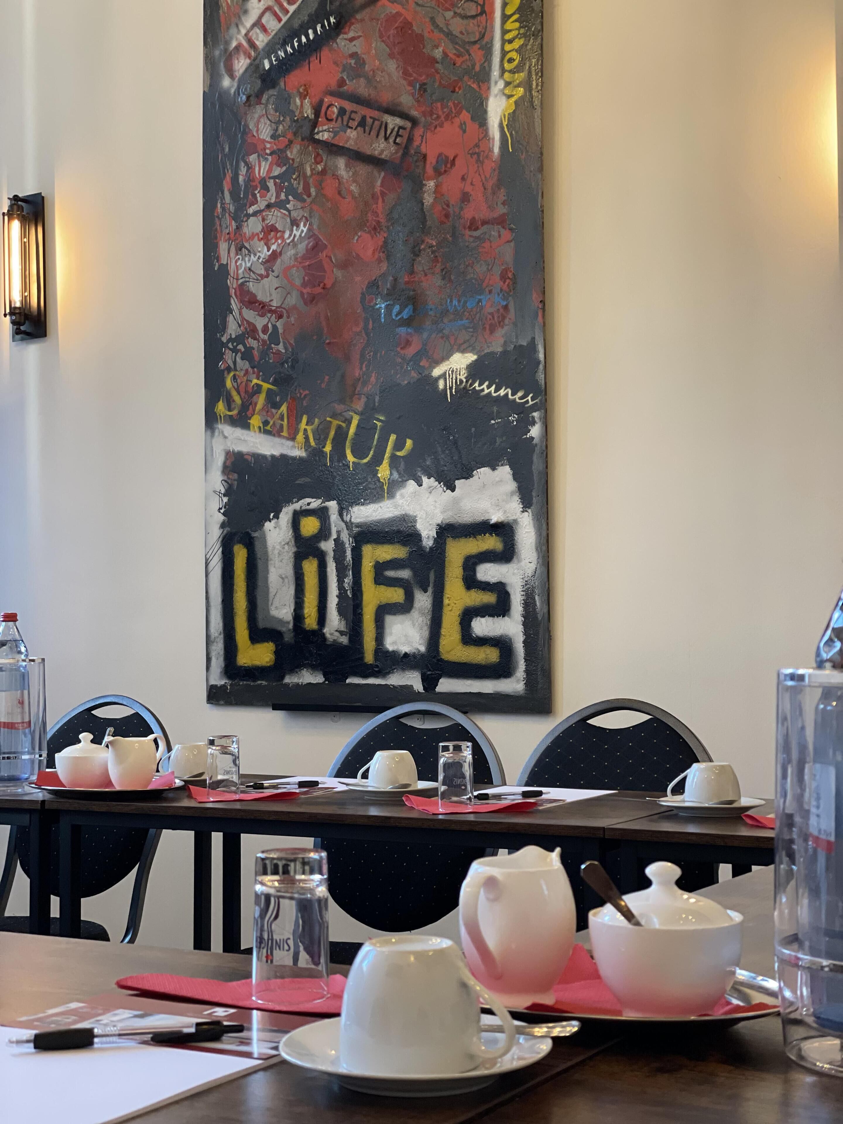 Un comedor con una mesa lista para dos personas, que incluye una lámpara de mesa moderna, un póster en la pared y un diseño de silla minimalista.