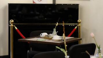 Un coin repas avec une table dressée pour deux personnes, un piano noir et des œuvres d’art encadrées accrochées au mur.