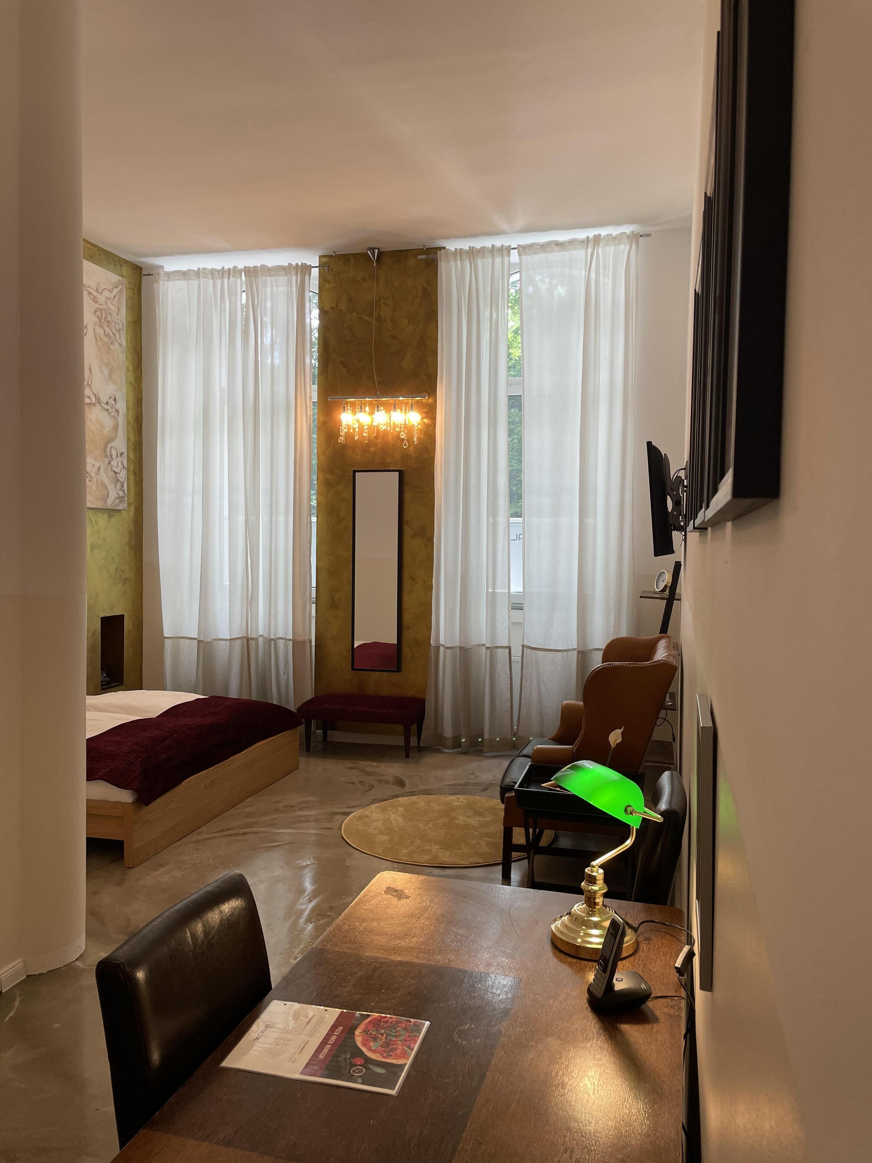 A hotel room with a bed, a seating area with a table and chairs, a large mirror, and a chandelier.