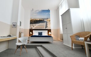 Un dormitorio con cama, escritorio, silla, armario y un gran mural de playa en la pared.