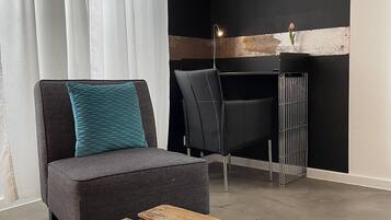 Ein modernes Wohnzimmer mit einem grauen Sofa, einem Holztisch, einem schwarzen Wand-Fernseher und einem schwarzen Schreibtisch mit Stuhl.