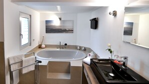 Un baño moderno con una bañera grande, un tocador con espejo y una ventana con persianas.