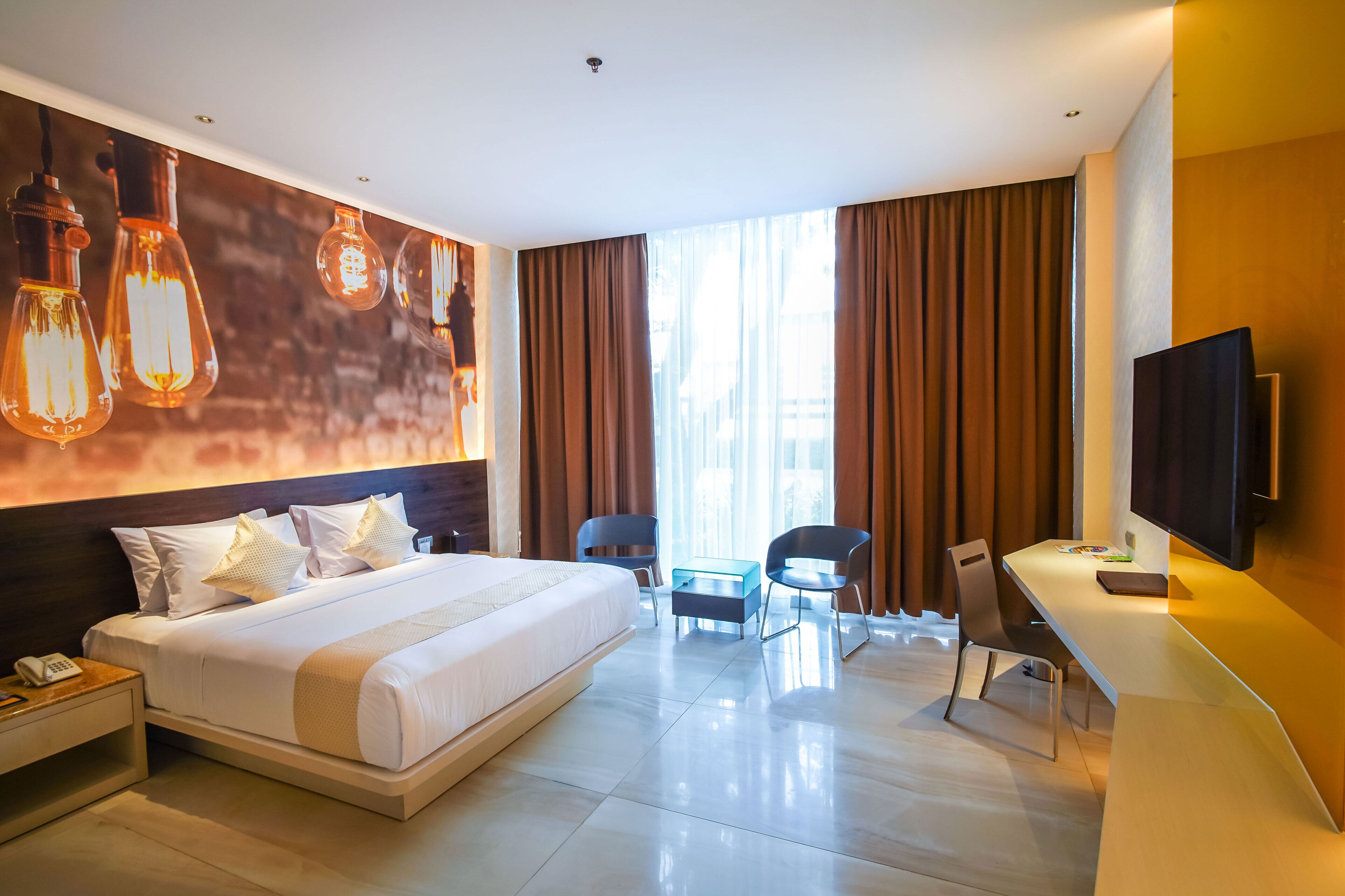A modern hotel room with a large bed, a desk with a chair, a television, and a window with curtains.