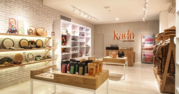 A modern retail store with wooden shelves displaying various products, a central display table with coffee bags, and a sign reading "kabo gift from Indonesia".