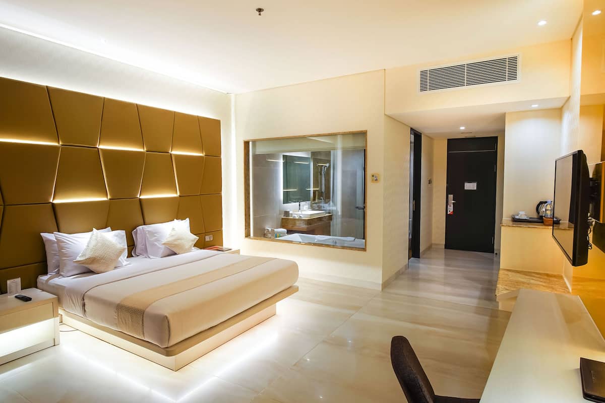 A modern hotel room with a large bed, bedside tables, a desk, and a large mirror.
